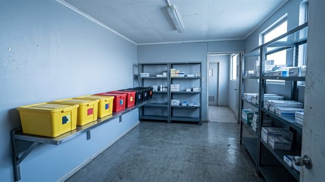 La misma sala de acopio ordenada: contenedores de colores separados por tipo de residuo, rotulados, sobre una repisa y con señalización en la pared.